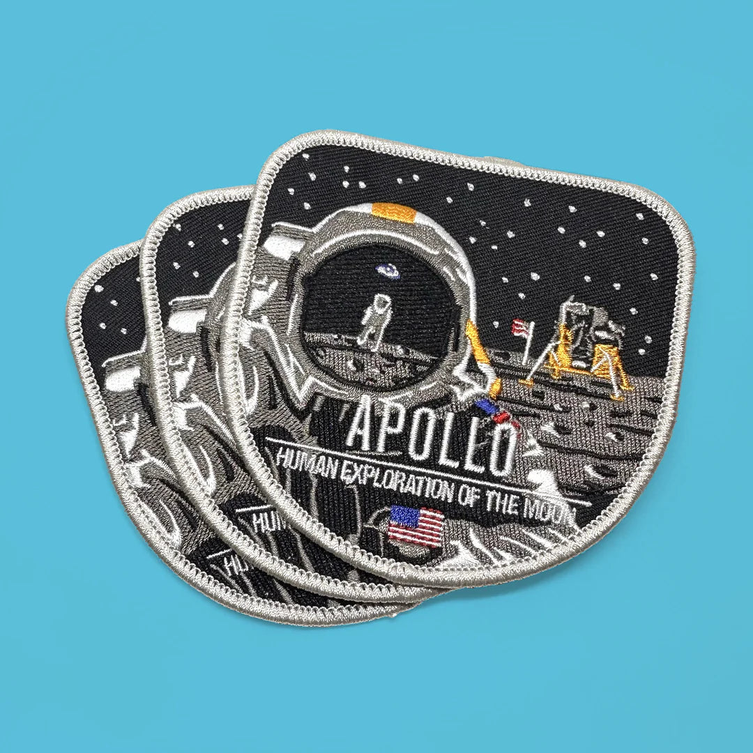Apollo moon landing embroidered patch by Thomas Romer at Chop Shop. Three overlapping patches featuring a black space background, white text reading 'APOLLO' and 'HUMAN EXPLORATION OF THE MOON,' and a small American flag detail on a bright blue background.
